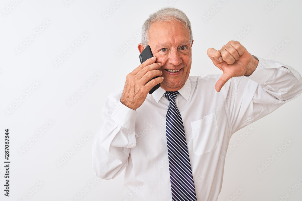 Senior grey-haired businessman talking on the smartphone over isolated white background with angry face, negative sign showing dislike with thumbs down, rejection concept Senior grey-haired businessman talking on the smartphone over isolated white background with angry face, negative sign showing dislike with thumbs down, rejection concept