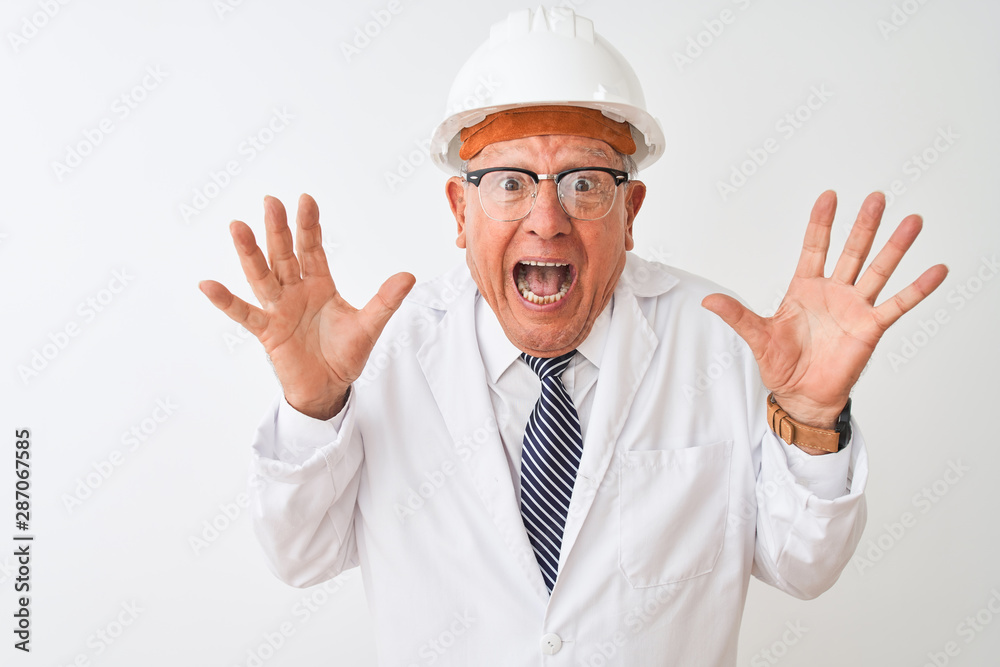 Senior grey-haired engineer man wearing coat and helmet over isolated white background celebrating crazy and amazed for success with arms raised and open eyes screaming excited. Winner concept Senior grey-haired engineer man wearing coat and helmet over isolated white background celebrating crazy and amazed for success with arms raised and open eyes screaming excited. Winner concept
