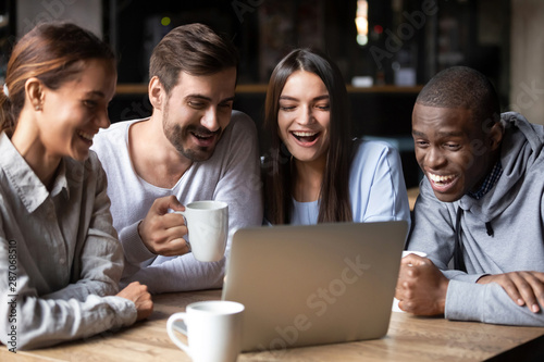 Happy multiracial friends watching funny comedy in cafe on laptop