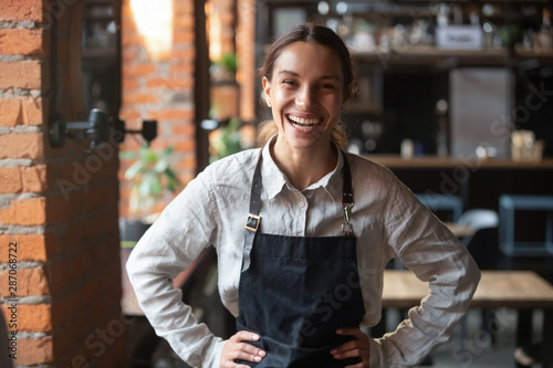 Cheerful young waitress wearing apron laughing looking at camera photo