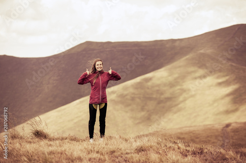 Girl hiker showing thumbs up while standing on the background of adorable mountains. Toned. © Андрей Репетий