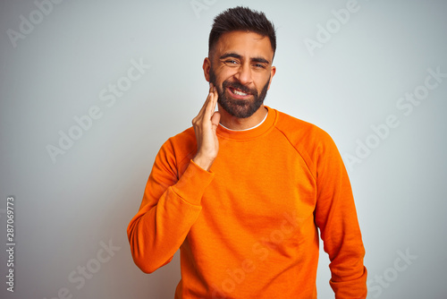 Young indian man wearing orange sweater over isolated white background touching mouth with hand with painful expression because of toothache or dental illness on teeth. Dentist concept. © Krakenimages.com