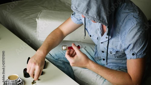 A hooded man sits on a white couch and smokes marijuana through a glass pipe. Concept of decriminalization of cannabis use