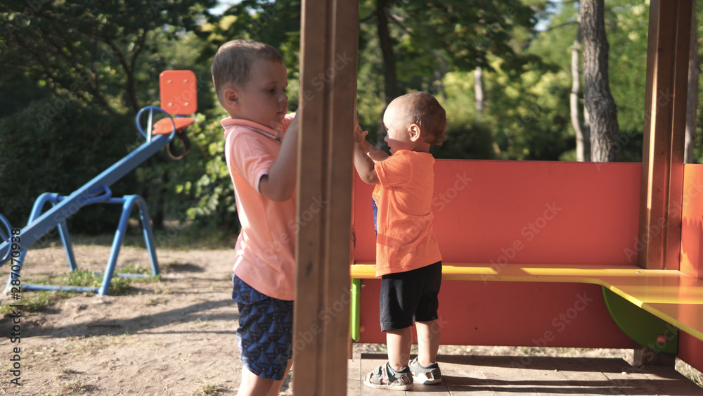 Fototapeta premium Two little boys playing on the playground with swing on the background