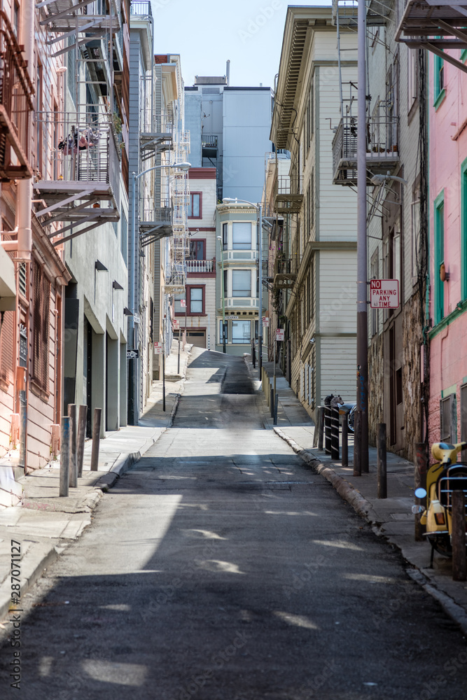 Narrow steep street in San Francisco with clean sidewalks and old fire escapes