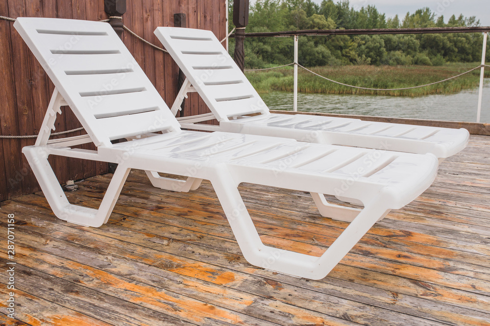 Two white sunbeds on a wooden pier by the river Two white sunbeds on a wooden pier by the river