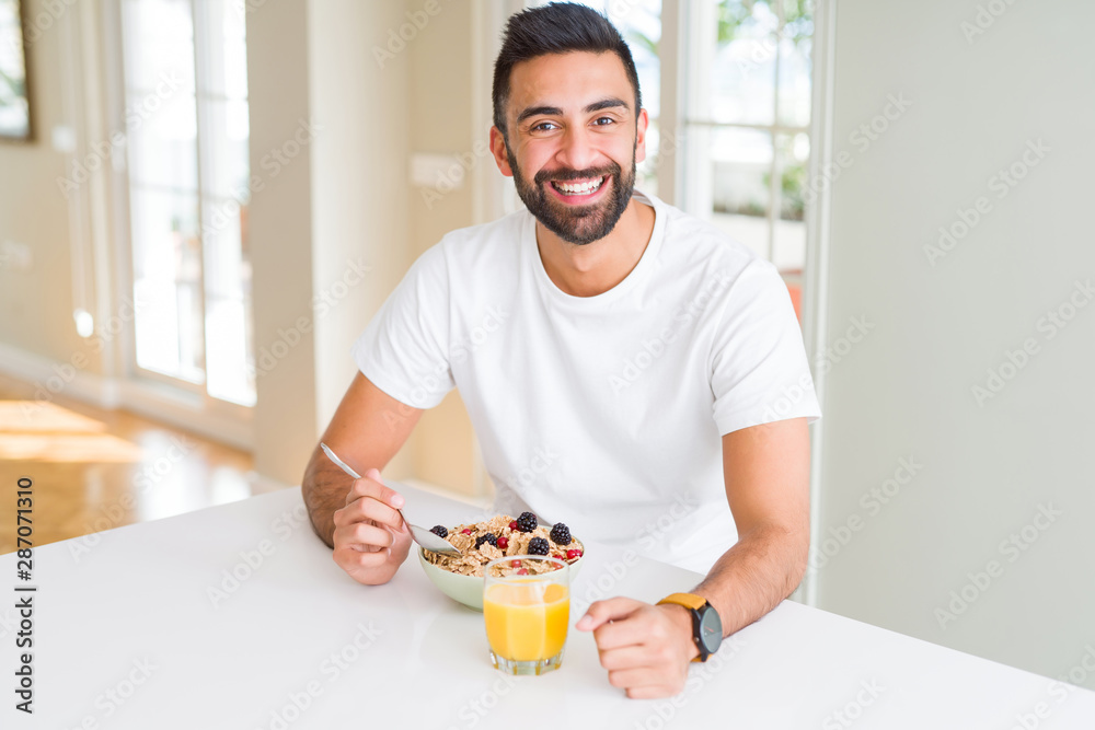 Handsome hispanic man eating healthy breakfast in the morning at home with a happy face standing and smiling with a confident smile showing teeth Handsome hispanic man eating healthy breakfast in the morning at home with a happy face standing and smiling with a confident smile showing teeth