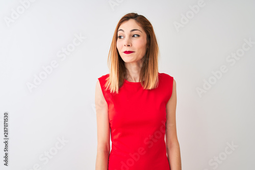 Redhead businesswoman wearing elegant red dress standing over isolated white background smiling looking to the side and staring away thinking. © Krakenimages.com