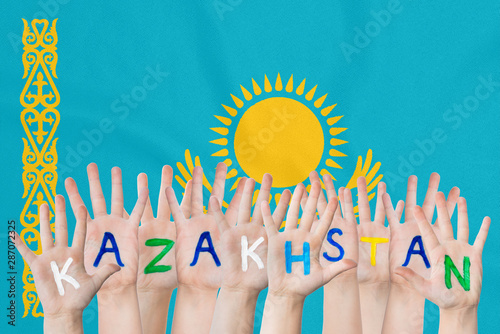 Inscription Kazakhstan on the children's hands against the background of a waving flag of the Kazakhstan photo