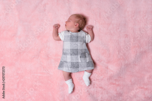 Sleeping newborn girl in a dress on a pink blanket. Top view. Space for text