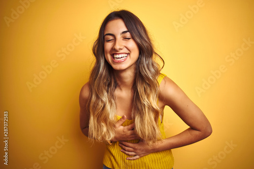 Young beautiful woman wearing t-shirt over yellow isolated background smiling and laughing hard out loud because funny crazy joke with hands on body.
