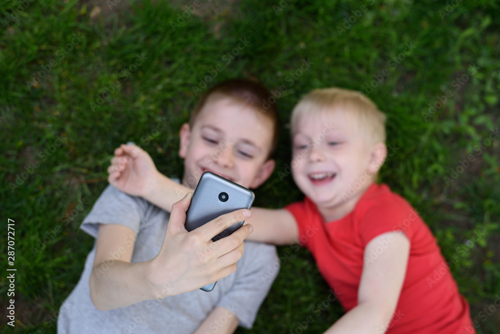 Two boys make selfie on a smartphone while lying on the grass. Top view Two boys make selfie on a smartphone while lying on the grass. Top view