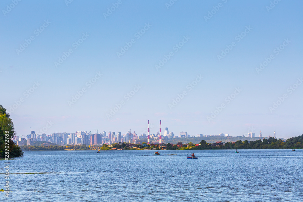 Summer sunny hot evening. Modern residential areas southern suburbs and midtown on hills in Kyiv on the right bank of the Dnipro River. Fishermen on boats on foreground. Kyiv. Ukraine. Aug. 28, 2019
