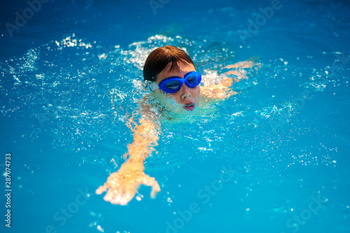 BOY WITH GOGGLES EXERCISING FREESTYLE SWIMMING AND BREATHING