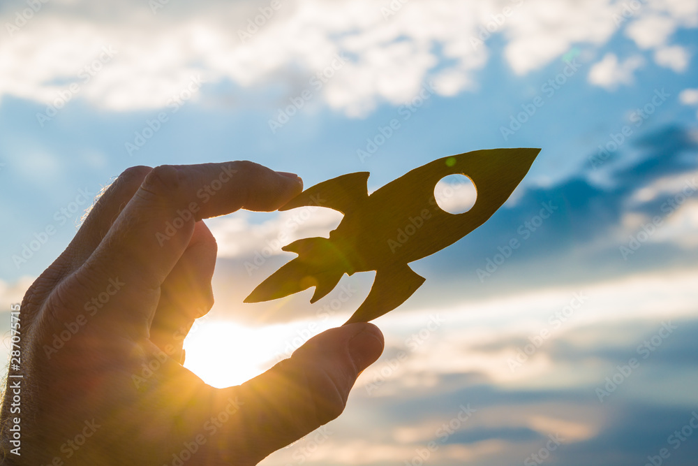 Rocket in hand on a background of the sky of the sun at sunset. On your marks. Concept business idea, success, take-off, promotion. - obrazy, fototapety, plakaty 