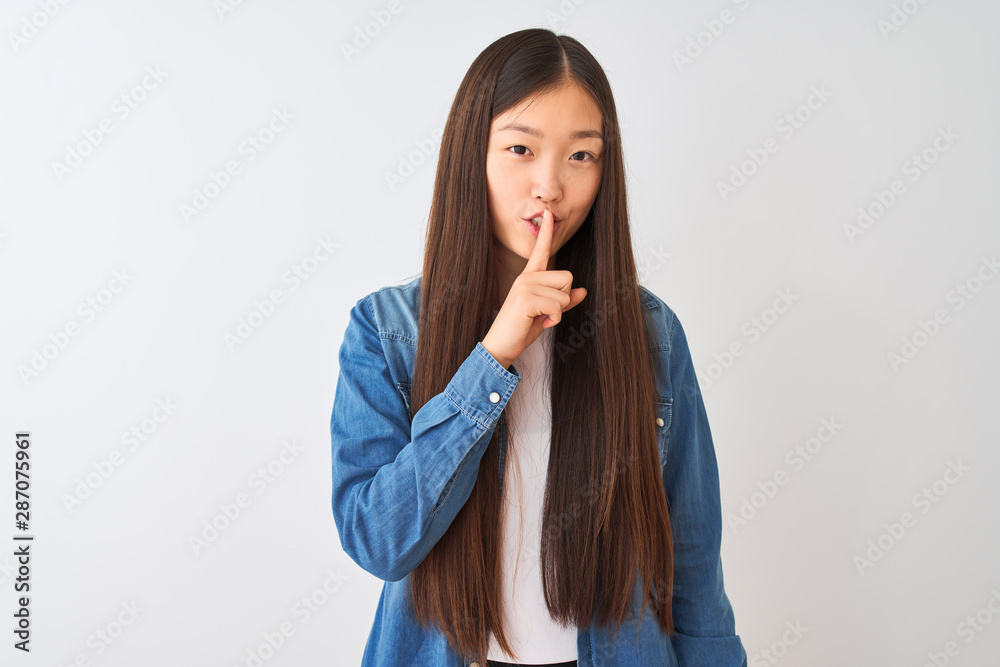 Young chinese woman wearing denim shirt standing over isolated white background asking to be quiet with finger on lips. Silence and secret concept. Young chinese woman wearing denim shirt standing over isolated white background asking to be quiet with finger on lips. Silence and secret concept.