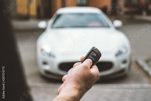 The man opens the car with a keychain, in the background is a white car.