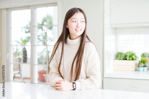Beautiful Asian woman wearing casual sweater looking away to side with smile on face, natural expression. Laughing confident.