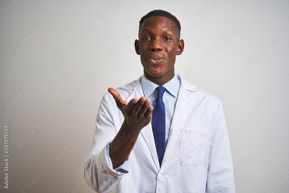 Young african american doctor man wearing coat standing over isolated white background looking at the camera blowing a kiss with hand on air being lovely and sexy. Love expression. Young african american doctor man wearing coat standing over isolated white background looking at the camera blowing a kiss with hand on air being lovely and sexy. Love expression.