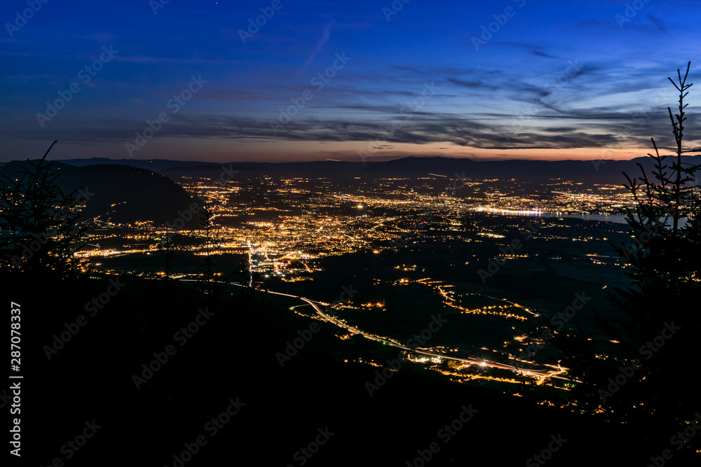 Evening top view of city lights, French Annemasse, Swiss Geneva,lake Geneva and picturesque sky with dark clouds after sunset,photo with long exposure.Department of Haute-Savoie in France.