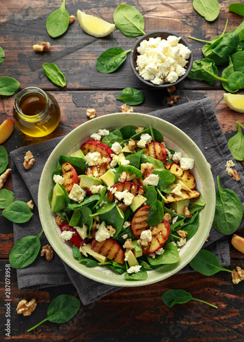 Summer Peach Salad with spinach, avocado, walnuts and feta cheese in rustic bowl. healthy food.