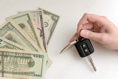 In a female hand the ignition key. Near dollars of various denominations. Concept - buying, renting a car