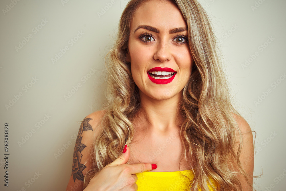 Young beautiful woman wearing yellow t-shirt standing over white isolated background with surprise face pointing finger to himself Young beautiful woman wearing yellow t-shirt standing over white isolated background with surprise face pointing finger to himself