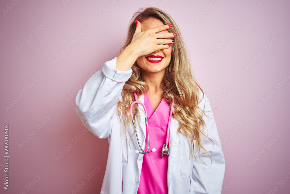 Young beautiful doctor woman using stethoscope over pink isolated background smiling and laughing with hand on face covering eyes for surprise. Blind concept. Young beautiful doctor woman using stethoscope over pink isolated background smiling and laughing with hand on face covering eyes for surprise. Blind concept.