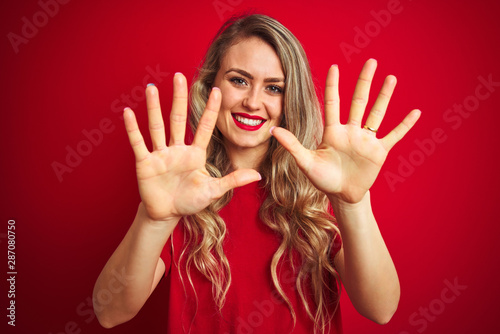 Young beautiful woman wearing basic t-shirt standing over red isolated background showing and pointing up with fingers number ten while smiling confident and happy. © Krakenimages.com