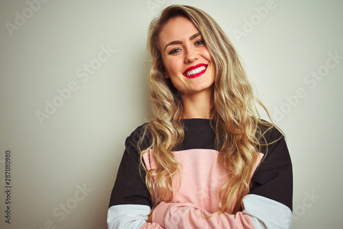 Young attractive woman wearing sweatshirt standing over white isolated background happy face smiling with crossed arms looking at the camera. Positive person.