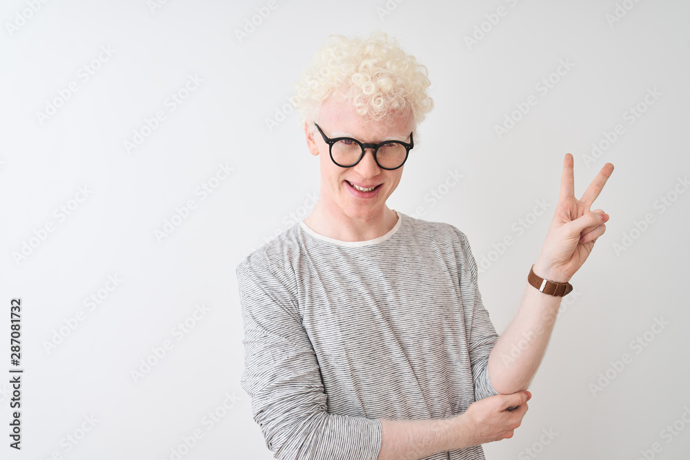 Young albino blond man wearing striped t-shirt and glasses over isolated white background smiling with happy face winking at the camera doing victory sign. Number two. Young albino blond man wearing striped t-shirt and glasses over isolated white background smiling with happy face winking at the camera doing victory sign. Number two.