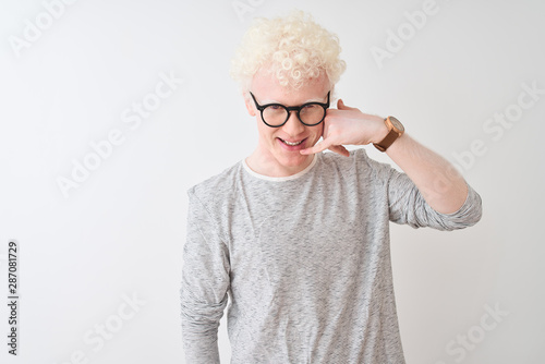 Young albino blond man wearing striped t-shirt and glasses over isolated white background smiling doing phone gesture with hand and fingers like talking on the telephone. Communicating concepts.