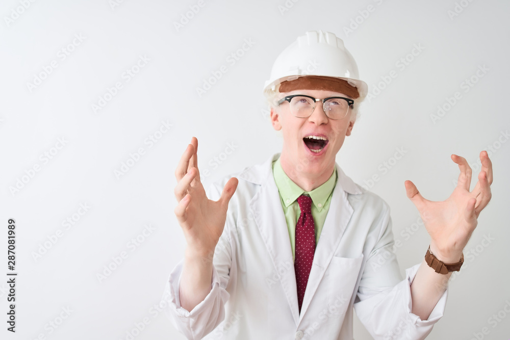 Albino scientist man wearing glasses and helmet standing over isolated white background crazy and mad shouting and yelling with aggressive expression and arms raised. Frustration concept.