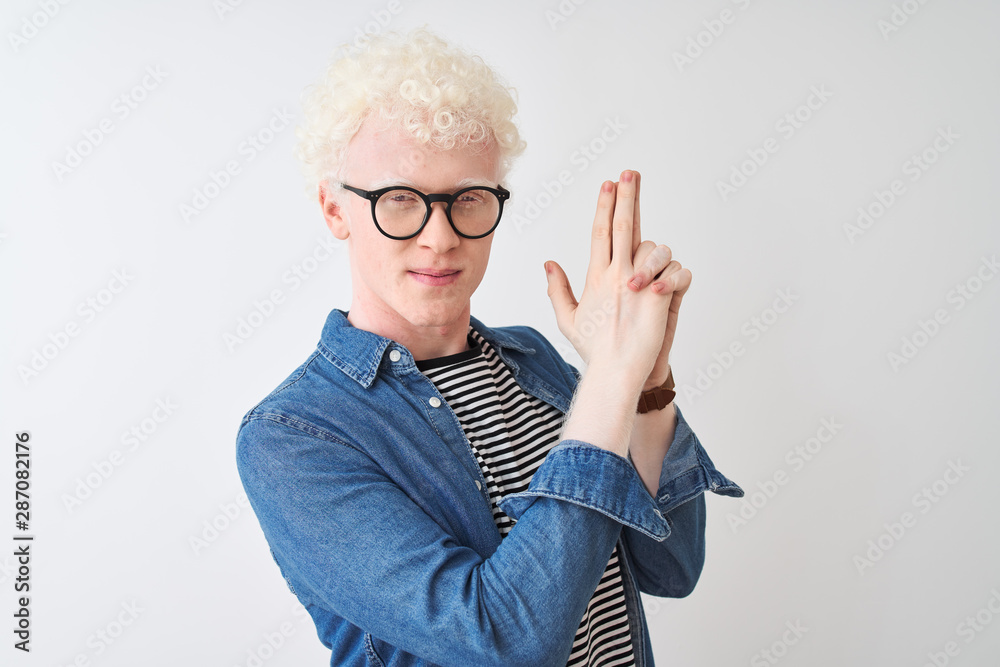 Young albino blond man wearing denim shirt and glasses over isolated white background Holding symbolic gun with hand gesture, playing killing shooting weapons, angry face Young albino blond man wearing denim shirt and glasses over isolated white background Holding symbolic gun with hand gesture, playing killing shooting weapons, angry face