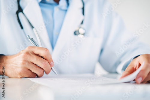 Close up of doctor reading and signing files and paperwork of patient photo