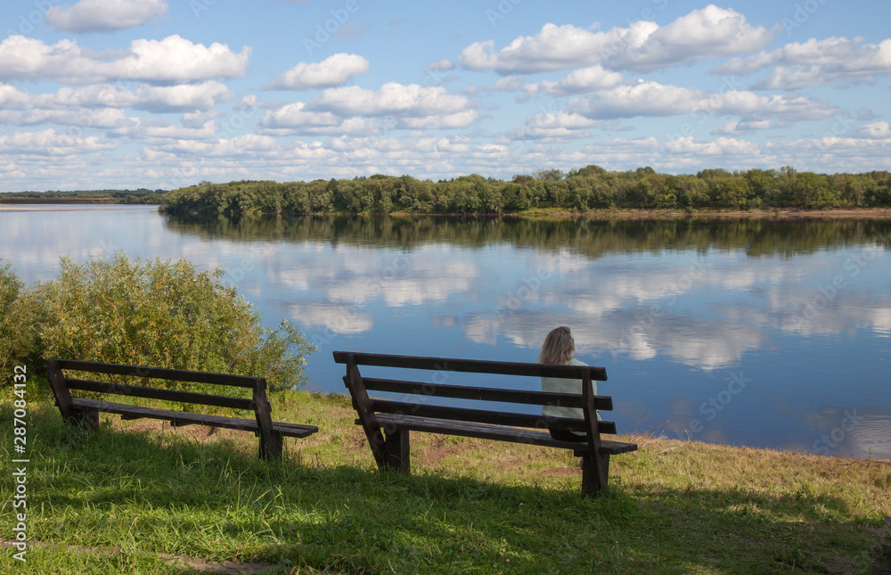 Beautiful landscape with river and clouds  and the girl on the bench