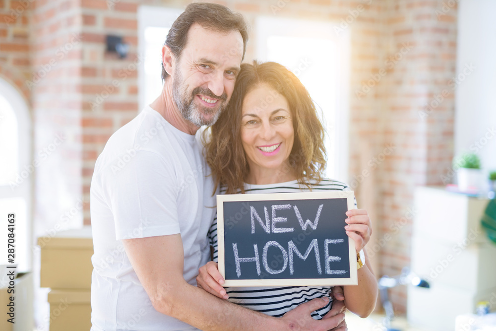 Middle age senior couple moving to a new house, smiling happy in love with apartmant holding a blackboard with new home text Middle age senior couple moving to a new house, smiling happy in love with apartmant holding a blackboard with new home text