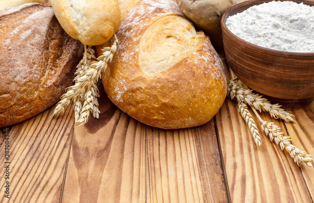 Loafs of bread with flour and wheat ears on wooden background. Loafs of bread with flour and wheat ears on wooden background.