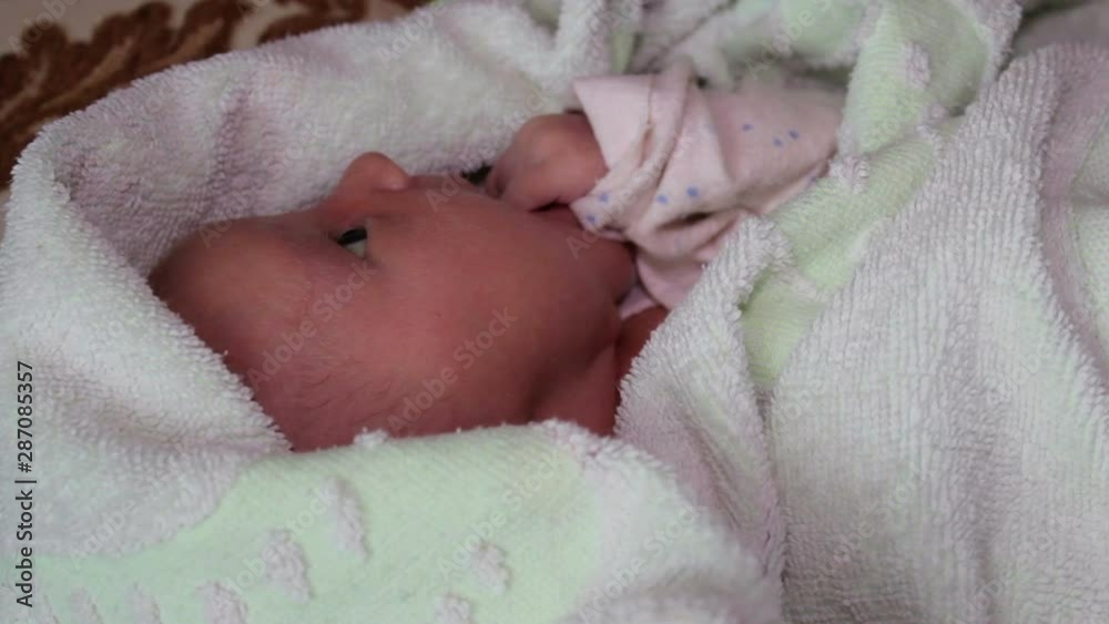 newborn baby in towel,baby holds his handles in his mouth and sucks, baby lies in a towel wrapped newborn baby in towel,baby holds his handles in his mouth and sucks, baby lies in a towel wrapped
