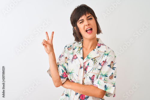 Beautiful woman on vacation wearing summer casual shirt over isolated white background smiling with happy face winking at the camera doing victory sign. Number two.