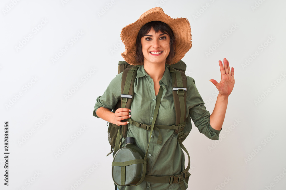 Hiker woman wearing backpack hat and water canteen over isolated white background showing and pointing up with fingers number five while smiling confident and happy. Hiker woman wearing backpack hat and water canteen over isolated white background showing and pointing up with fingers number five while smiling confident and happy.