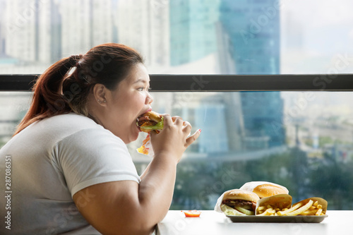 Bild auf Leinwand Voracious fat woman eating burger in the restaurant
