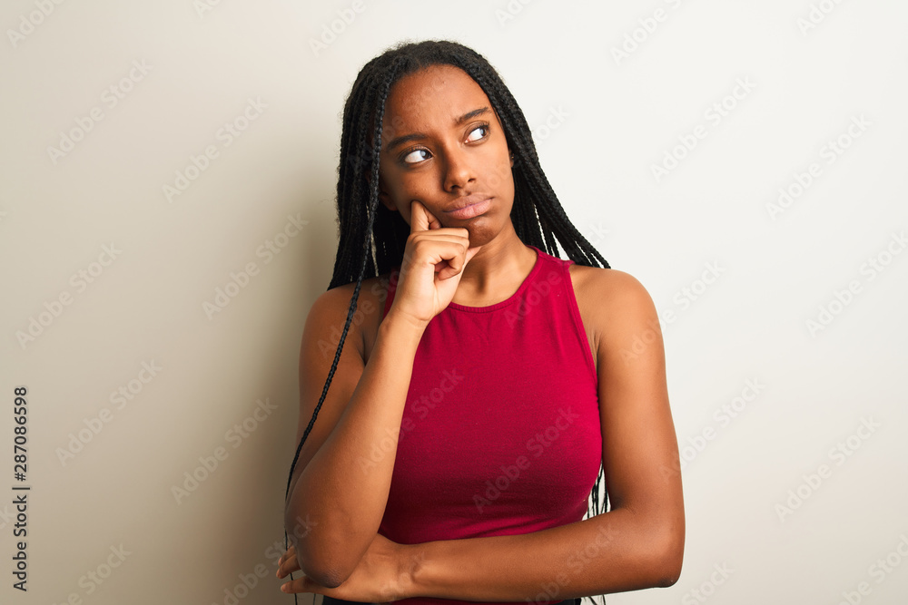 African american woman wearing red casual t-shirt standing over isolated white background with hand on chin thinking about question, pensive expression. Smiling with thoughtful face. Doubt concept. African american woman wearing red casual t-shirt standing over isolated white background with hand on chin thinking about question, pensive expression. Smiling with thoughtful face. Doubt concept.
