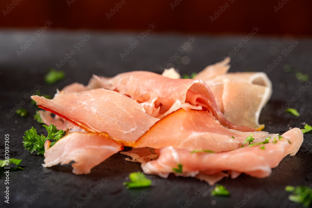 Thin sliced smoked pork ham on a dark slate
