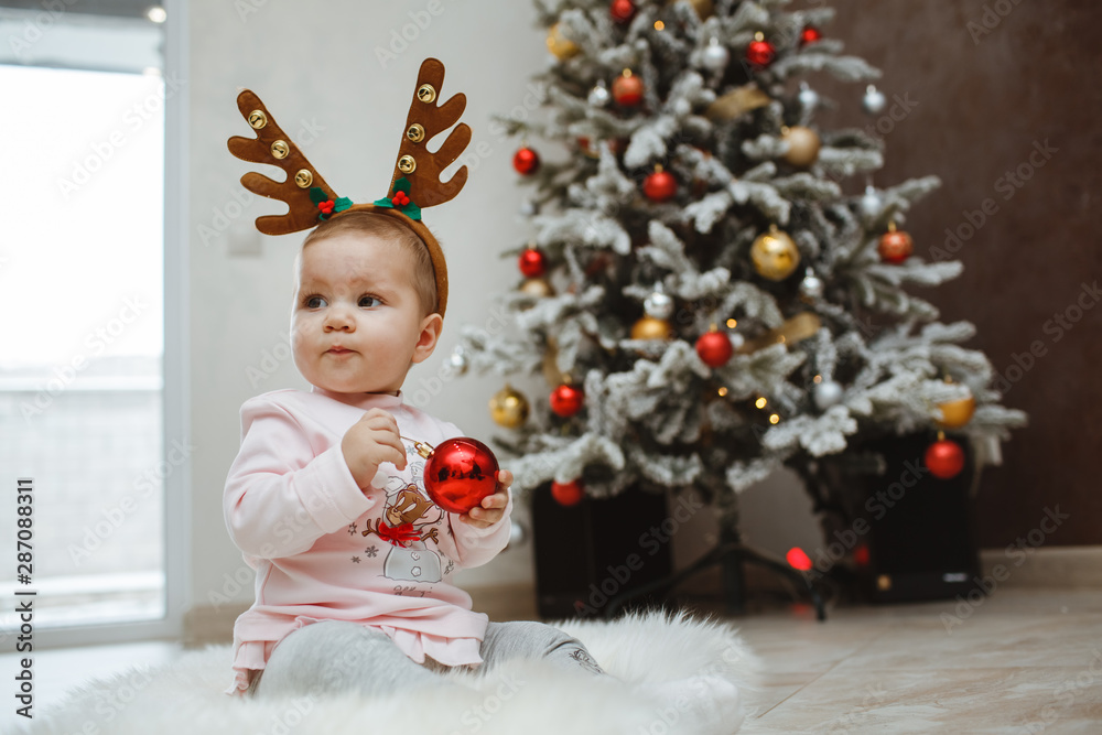 Fototapeta premium Happy child with deer horns near a Christmas tree.