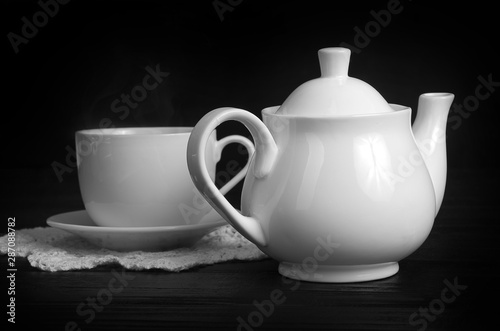 cup of hot tea and white teapot on a black table