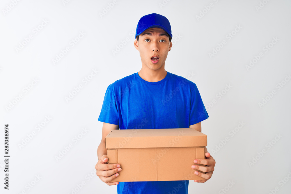 Chinese deliveryman wearing cap holding box standing over isolated white background scared in shock with a surprise face, afraid and excited with fear expression Chinese deliveryman wearing cap holding box standing over isolated white background scared in shock with a surprise face, afraid and excited with fear expression