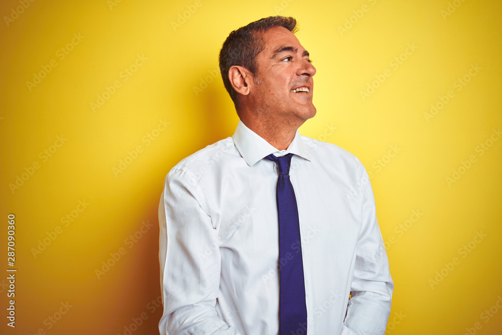 Handsome middle age businessman standing over isolated yellow background looking away to side with smile on face, natural expression. Laughing confident. Handsome middle age businessman standing over isolated yellow background looking away to side with smile on face, natural expression. Laughing confident.