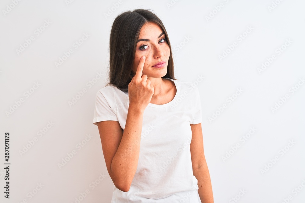 Young beautiful woman wearing casual t-shirt standing over isolated white background Pointing to the eye watching you gesture, suspicious expression Young beautiful woman wearing casual t-shirt standing over isolated white background Pointing to the eye watching you gesture, suspicious expression