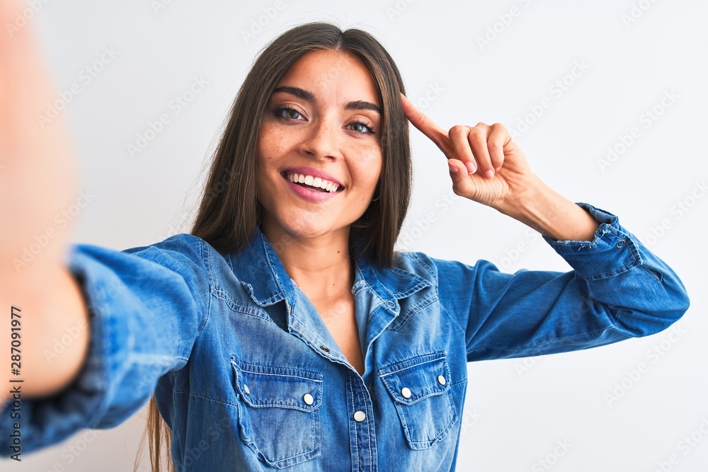 Beautiful woman wearing denim shirt make selfie by camera over isolated white background Smiling pointing to head with one finger, great idea or thought, good memory Beautiful woman wearing denim shirt make selfie by camera over isolated white background Smiling pointing to head with one finger, great idea or thought, good memory